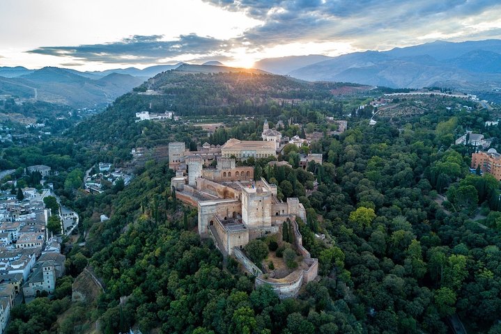 Aerial view of the Alhambra’s towers and wooded hill beneath the mountains