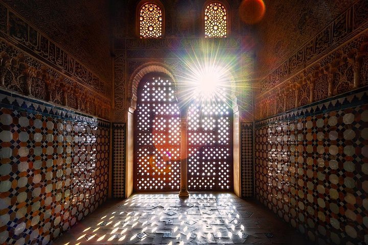 Sunlight streaming through patterned windows into a tiled Nasrid palace room