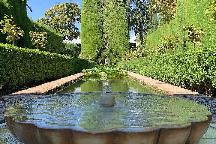 A stone fountain and long pool between clipped Generalife hedges