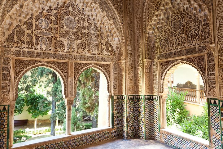Decorated Nasrid arches and tiled walls overlooking a green courtyard