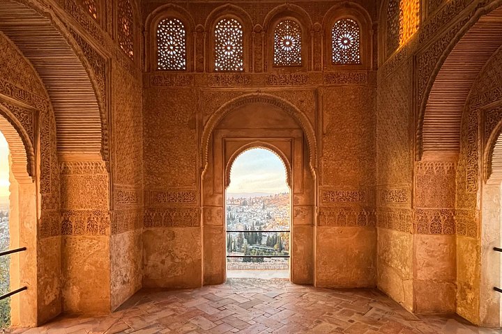 Warm light on carved arches and patterned walls inside an Alhambra palace room