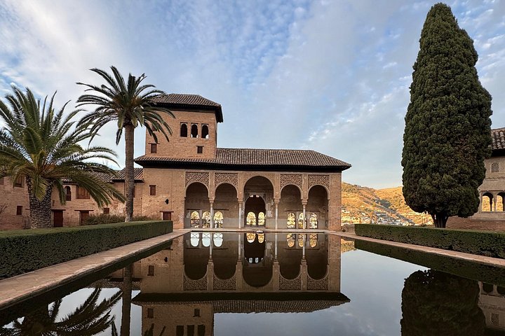 Partal Palace and its arches reflected in a long pool beside a palm tree