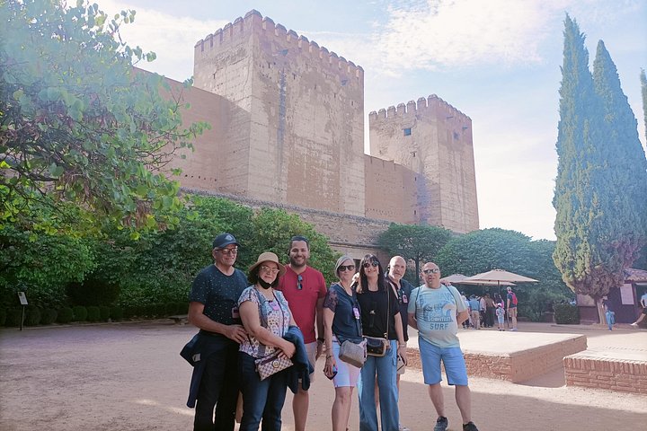 Visitors beside brick Alhambra towers, cypress trees and clipped hedges