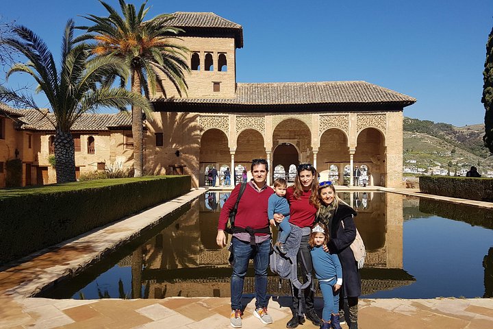 Visitors beside the Partal reflecting pool, with a palm tree and arched pavilion behind