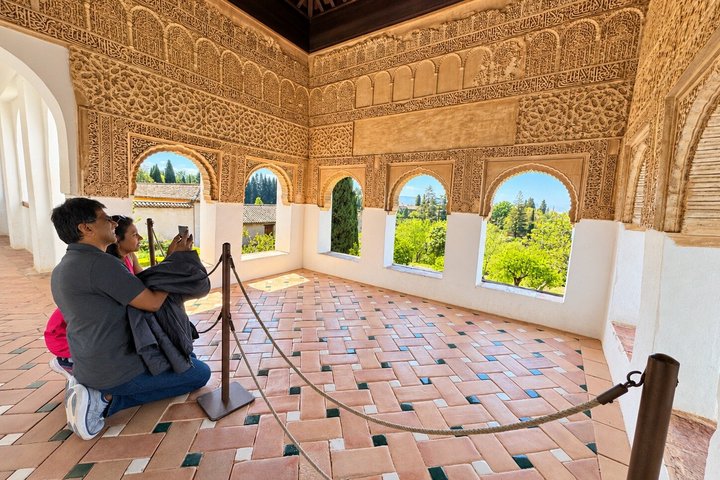 Visitors beside decorated walls and windows in the Nasrid Palaces